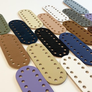 May include: A selection of oval bag bases in colours such as white, black, blue, and beige. Each base has evenly spaced holes for stitching and a textured or smooth finish. These bases are ideal for crafting.