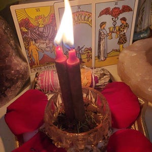 May include: A still-life image featuring lit red candles in a glass bowl, surrounded by red rose petals. Tarot cards with the words "THE LOVE" and "Love" are visible. The scene evokes a spiritual or romantic theme.