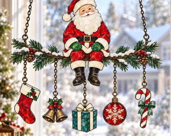 May include: A hanging stained glass-style ornament featuring Santa Claus sitting on a pine branch. Below the branch, five charms hang from chains: a red stocking, two gold bells, a blue gift box, a red snowflake bauble, and a candy cane.