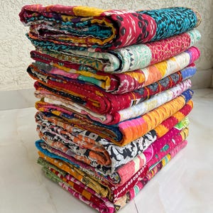 May include: A pile of vibrant patchwork quilts. The quilts display a range of patterns and colours, including red, blue, yellow, and pink. The quilts are neatly folded, highlighting the detailed stitching and design.
