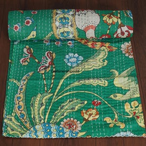 May include: A rolled-up green quilt with a vibrant floral pattern. The design features large, stylized flowers and leaves in shades of yellow, red, blue, and white, all set against a green background. The quilt is hand-stitched with white thread.