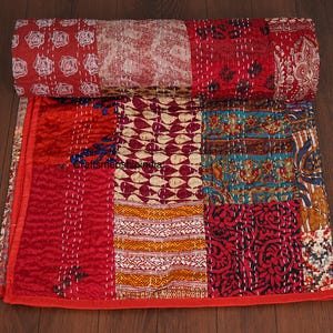 May include: A patchwork quilt with a variety of patterns and colors. The quilt features red, burgundy, teal, and cream-colored patches. The quilt is rolled up at the top, showing the different patterns and textures. The quilt is made of fabric and has a stitched design.