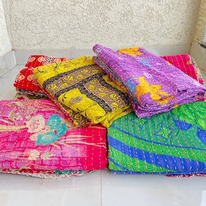 May include: A collection of colorful, patterned quilts. The quilts are folded and stacked, showcasing a variety of designs and colors, including red, yellow, pink, purple, and green. The quilts appear to be made of soft fabric.