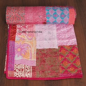 Puede incluir: Un edredón de patchwork en tonos rosa, rojo y crema, con varios cuadrados de tela estampada. El edredón está cosido a mano con hilo blanco y tiene una sección enrollada. El texto "craftsmanshipindia" es visible.