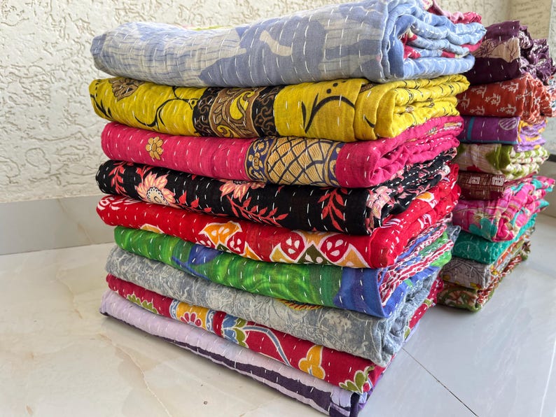 Pu&ograve; includere: Una pila di trapunte colorate e piegate. Le trapunte mostrano una variet&agrave; di motivi e colori, tra cui giallo, rosa, rosso, verde e blu. Ogni trapunta &egrave; fatta di tessuto e ha un design cucito.