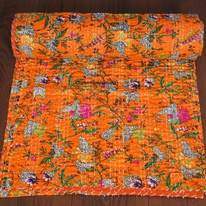 May include: An orange floral quilt with a rolled edge. The quilt features a repeating pattern of white, pink, purple, and green flowers and leaves. The quilt is made of a soft, quilted fabric.