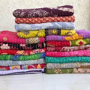 Pu&ograve; includere: Pile di trapunte colorate e decorate. Le trapunte presentano una variet&agrave; di disegni e colori, tra cui rosa, rosso, viola, giallo e verde. Ogni trapunta &egrave; piegata e impilata ordinatamente, mostrando gli intricati motivi e le trame.