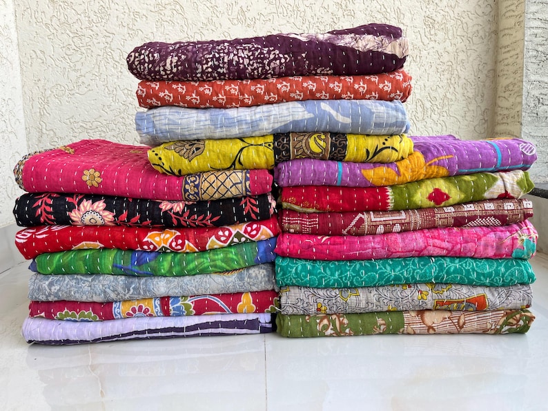 Pu&ograve; includere: Pile di trapunte colorate e decorate. Le trapunte presentano una variet&agrave; di disegni e colori, tra cui rosa, rosso, viola, giallo e verde. Ogni trapunta &egrave; piegata e impilata ordinatamente, mostrando gli intricati motivi e le trame.