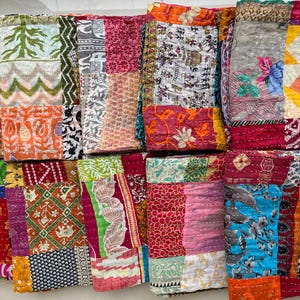 May include: A selection of vibrant, patchwork fabric items. The textiles display a range of patterns, including floral, geometric, and abstract designs. The colour palette includes reds, oranges, greens, blues, and pinks. The items appear to be quilted or stitched together.