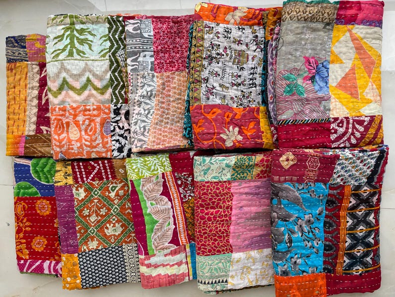 May include: A selection of vibrant, patchwork fabric items. The textiles display a range of patterns, including floral, geometric, and abstract designs. The colour palette includes reds, oranges, greens, blues, and pinks. The items appear to be quilted or stitched together.
