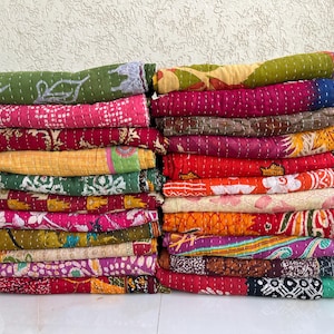 以下が含まれることがあります： カラフルなキルトブランケットが2つの山に。ピンク、緑、黄色、赤など、さまざまな模様と色があります。ブランケットはきちんと積み重ねられており、さまざまなデザインと質感が示されています。