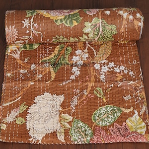 May include: Rolled brown quilt with a floral pattern in white, green, and pink. The quilt features a repeating design of large flowers and leaves, with the text "Craftsmanshipindia" visible. The quilt is stitched with white thread.