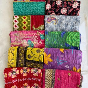Pu&ograve; includere: Una collezione di trapunte kantha piegate e colorate. Le trapunte presentano una variet&agrave; di motivi, tra cui floreali, paisley e geometrici. La tavolozza dei colori comprende rosso, verde, giallo, viola e rosa, con cuciture intricate.