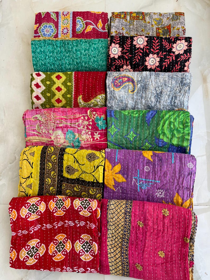 Pu&ograve; includere: Una collezione di trapunte kantha piegate e colorate. Le trapunte presentano una variet&agrave; di motivi, tra cui floreali, paisley e geometrici. La tavolozza dei colori comprende rosso, verde, giallo, viola e rosa, con cuciture intricate.