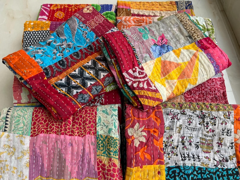 May include: A selection of vibrant patchwork quilts. Each quilt is made from a variety of fabrics in shades of red, blue, orange, and pink. The quilts are stitched together with visible seams, giving a textured look. The overall theme is bohemian and handmade.