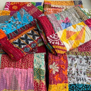 Pode incluir: Uma coleção de colchas de retalhos coloridas. Cada colcha apresenta uma combinação única de tecidos em vários padrões e cores, incluindo vermelho, azul, laranja e amarelo. As colchas estão empilhadas, mostrando suas intrincadas costuras e design.