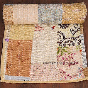 May include: A patchwork quilt with a variety of patterned fabrics in shades of beige, gold, brown, and blue. The quilt is hand-stitched with visible white thread and features floral and paisley designs. The text "Craftsmenshipindia" is visible on the quilt.