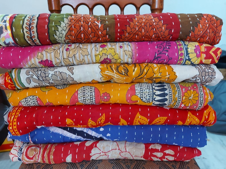 Puede incluir: Una pila de edredones coloridos y estampados. Los edredones presentan varios dise&ntilde;os, incluidos patrones florales y geom&eacute;tricos, en tonos de rojo, rosa, amarillo, verde y azul. Cada edred&oacute;n est&aacute; doblado y apilado uno encima del otro.