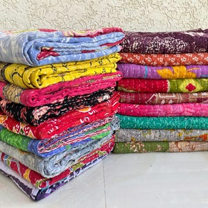 Pu&ograve; includere: Pile di trapunte colorate e piegate. Le trapunte presentano una variet&agrave; di motivi e colori, tra cui blu, giallo, rosa e rosso. Ogni trapunta &egrave; unica, con cuciture visibili e un design patchwork. Le trapunte sono impilate ordinatamente.
