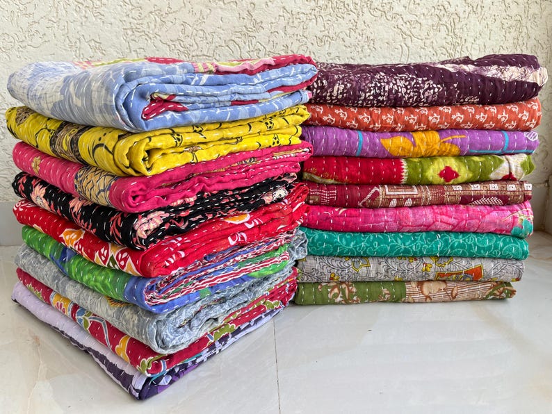 Pu&ograve; includere: Pile di trapunte colorate e piegate. Le trapunte presentano una variet&agrave; di motivi e colori, tra cui blu, giallo, rosa e rosso. Ogni trapunta &egrave; unica, con cuciture visibili e un design patchwork. Le trapunte sono impilate ordinatamente.
