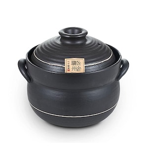 May include: A black ceramic cooking pot with a matching lid. The pot has two handles and a white accent line. The lid has a small opening and a label with text. The pot is designed for cooking.