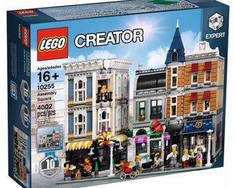 May include: A LEGO Creator Expert Assembly Square building set. The box features a detailed illustration of a multi-story building with shops and apartments. The set includes 4002 pieces and is for ages 16+. The box has the LEGO and Creator logos.