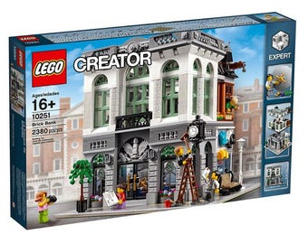 May include: A LEGO Creator Brick Bank building set, featuring a detailed facade with green window frames, a clock, and miniature figures. The box indicates the set is for ages 16+ and contains 2380 pieces.