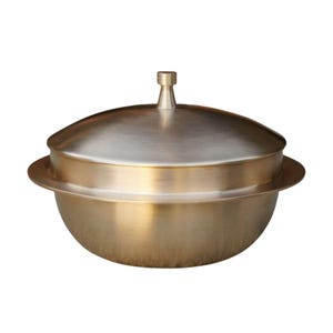 May include: A metallic gold-toned lidded pot with a smooth, brushed finish. The vessel features a rounded bowl-shaped base, a wide horizontal rim extending from the center, and a domed lid topped with a small, cylindrical handle knob.