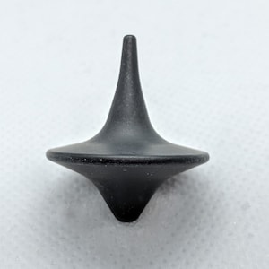 Può includere: Una trottola nera con una punta appuntita e una base larga.