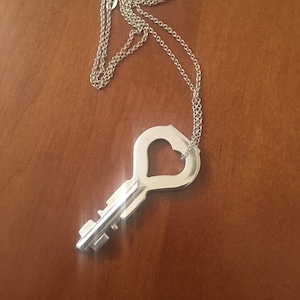May include: A silver key necklace with a heart-shaped keyhole. The chain is a delicate silver chain.