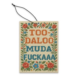 May include: A rectangular air freshener featuring the text "TOO-DALOO MUDA FUCKA" in orange and blue cross-stitch style. The text is framed by a floral border of red, blue, and green flowers and leaves. A black string is attached.