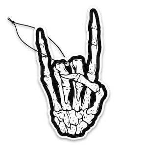 May include: Black and white air freshener in the shape of a skeleton hand making the rock and roll hand gesture. The air freshener has a black string attached for hanging.