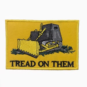 May include: Embroidered patch showing a yellow bulldozer with a black cab and blade, set against a yellow background. The text "TREAD ON THEM" is embroidered in black at the bottom. The patch has a yellow border.