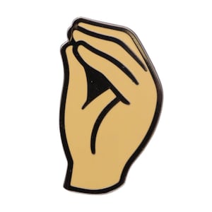 May include: A pin featuring a stylized hand gesture, with fingers pinched together. The pin has a tan background with black outlines and details. The hand gesture is a common Italian expression.