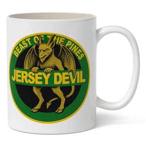 Puede incluir: Taza de cerámica blanca con un diseño circular verde y negro. El texto dice "BEAST OF THE PINES" y "JERSEY DEVIL". El diseño presenta una ilustración amarilla de una criatura alada y con cuernos.
