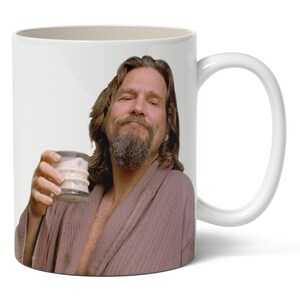 May include: White ceramic coffee mug featuring a portrait of a man holding a drink. The man has a beard and is wearing a robe. The mug has a white handle and a white interior.