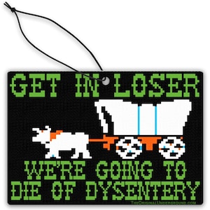 Puede incluir: Ambientador negro con diseño pixelado de carro y buey. El texto verde dice "GET IN LOSER WE'RE GOING TO DIE OF DYSENTERY". El ambientador tiene una cuerda negra para colgar.