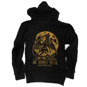 May include: Black hoodie featuring a gold illustration of a winged creature howling at the moon, with the text "THE JERSEY DEVIL BEAST OF THE PINES". The design includes skulls and bones.