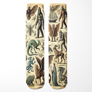 Puede incluir: Un par de calcetines color crema con una ilustración vintage de varias criaturas míticas y críptidos. El diseño incluye imágenes de Bigfoot, dragones y otros seres fantásticos en tonos marrones, verdes y azules.