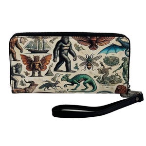 May include: A rectangular wallet with a black zip and wrist strap. The wallet has a cream background with illustrations of mythical creatures, including Bigfoot, a dragon, and a winged insect. The illustrations are in shades of brown, green, and blue.