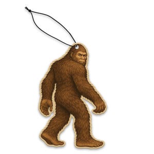 Puede incluir: Un ambientador de madera con forma de Bigfoot marrón, con una cuerda negra para colgarlo. El Bigfoot se representa caminando, con detalles de pelaje y rasgos faciales. El ambientador está diseñado para colgarlo en un coche o habitación.