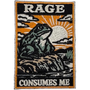 Könnte beinhalten: Gestickter Aufnäher mit einem Froschdesign. Der Aufnäher zeigt einen Frosch, der auf einem Felsen sitzt, mit einem Sonnenuntergang im Hintergrund. Der Text "RAGE" steht oben und "CONSUMES ME" unten. Der Aufnäher hat einen orangefarbenen Rand.