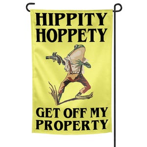 Może przedstawiać: Żółta flaga ogrodowa z napisem "HIPPITY HOPPETY GET OFF MY PROPERTY". Flaga przedstawia żabę w koszuli, spodniach i szelkach, trzymającą broń. Żaba stoi przed trawą.
