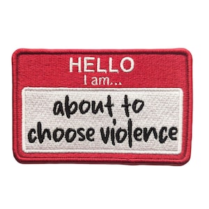 Puede incluir: Un parche bordado rojo con las palabras "HELLO I am..." en la parte superior y "about to choose violence" en negro sobre un fondo blanco. El parche tiene forma rectangular.