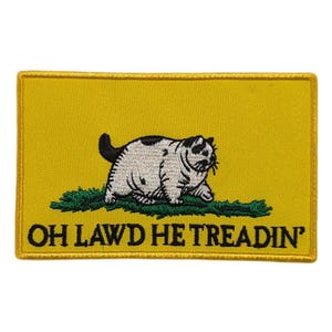 Op de afbeelding: Geborduurde patch met een cartoonkat op een gele achtergrond. De kat is wit met zwarte vlekken en zit op groen gras. De tekst "OH LAWD HE TREADIN'" staat onder de kat.