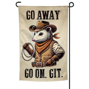 May include: A garden flag featuring a cartoon opossum dressed as a cowboy, complete with a hat, vest, and bandana. The flag has the text "GO AWAY" at the top and "GO ON. GIT." at the bottom. The opossum is holding a lasso.