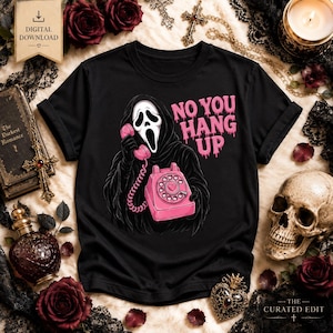 May include: A black t-shirt featuring a graphic of a hooded figure with a white mask holding a pink rotary telephone. The text "NO YOU HANG UP" is printed in pink above the phone. The figure is wearing a black robe with detailed shading.