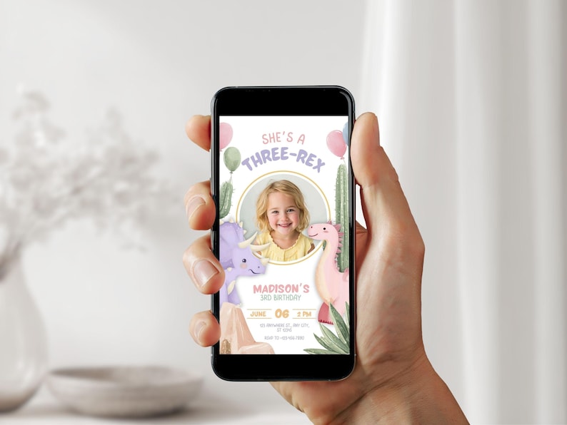 May include: A smartphone displays a birthday invitation with a child's photo. The design features a dinosaur theme with the text "She's a Three-Rex" and "Madison's 3rd Birthday". Pink and green balloons and cacti are also included.