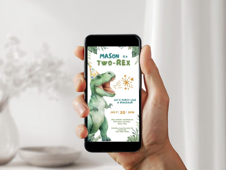 May include: A smartphone displays a birthday invitation with a watercolor illustration of a green Tyrannosaurus Rex wearing a party hat. The invitation reads "Mason is a Two-Rex" with party details and a request to RSVP.