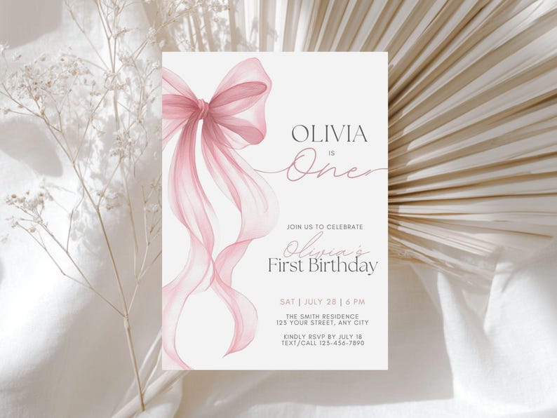 Peut inclure: Une invitation d'anniversaire rose clair avec un n&oelig;ud et des rubans &agrave; l'aquarelle. Le texte indique "Olivia a un an" et "Premier anniversaire d'Olivia". Les d&eacute;tails incluent la date, l'heure, le lieu et les informations RSVP. L'invitation est sur fond neutre.